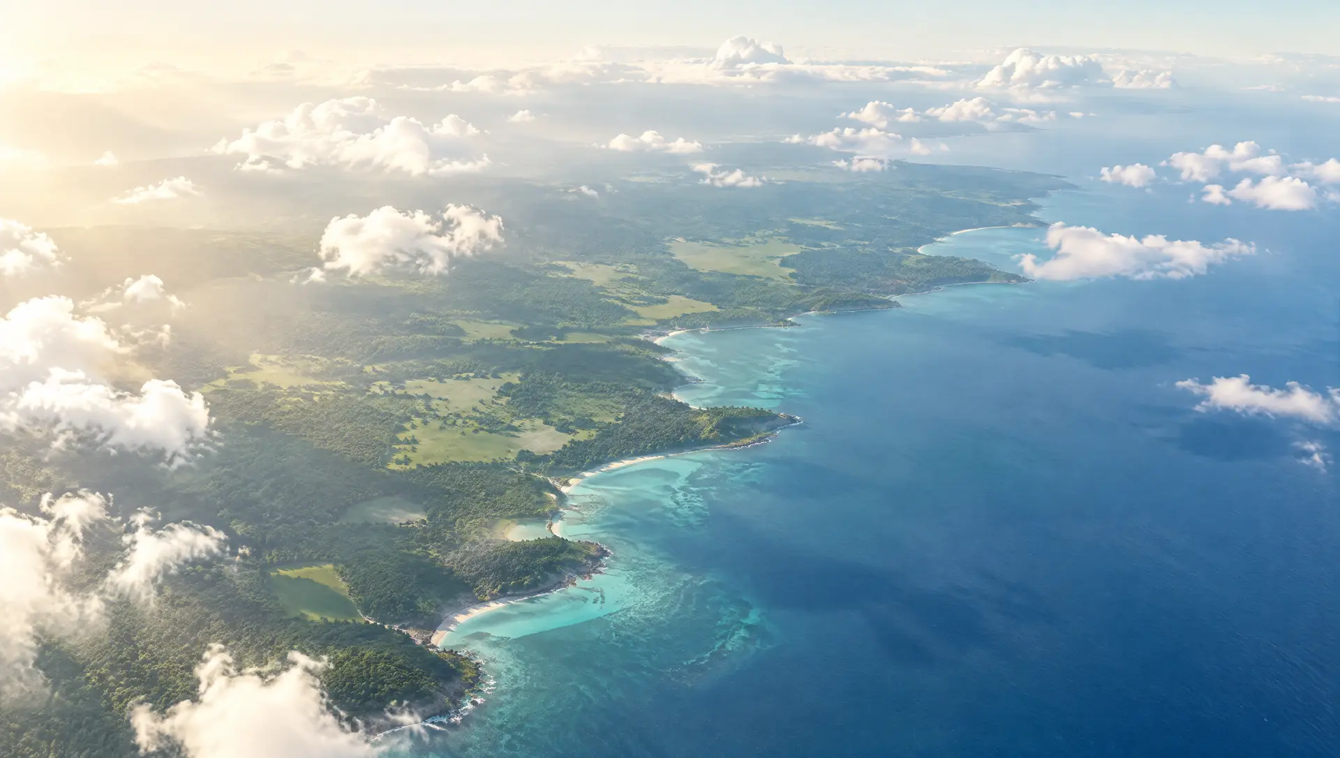 A green coastline meeting a turquoise ocean, seen from high above.